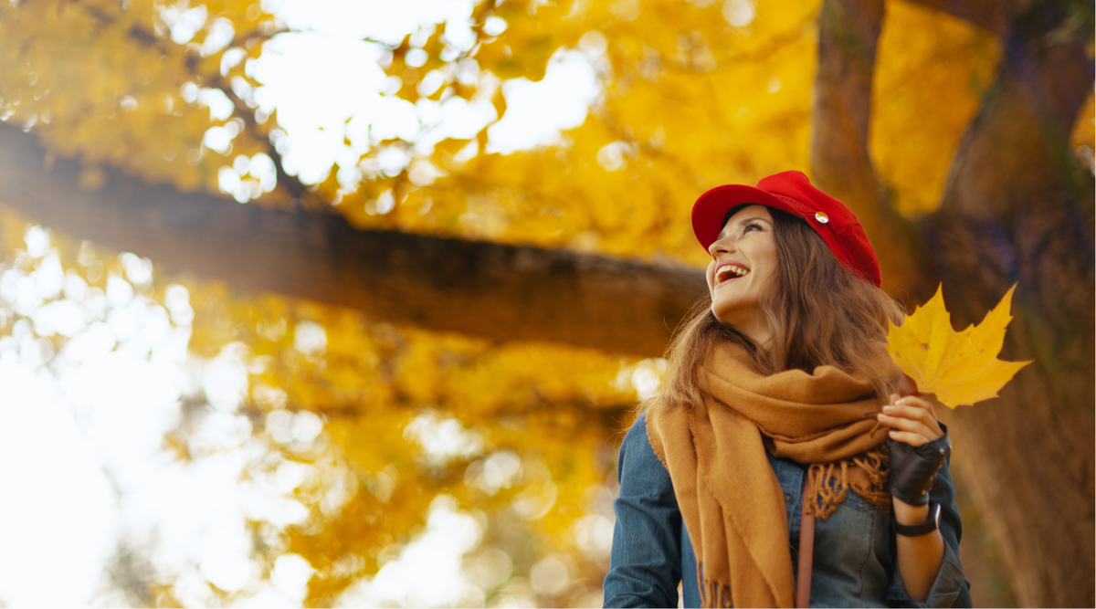 • Frau mit warmer Herbstjacke lächelt beim Spaziergang